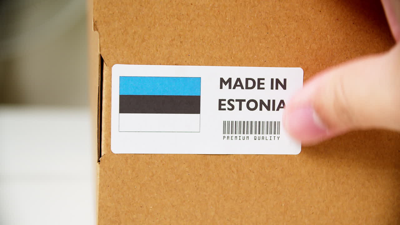 Hands applying MADE IN ESTONIA flag label on a shipping cardboard box with products
