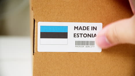 hands applying made in estonia flag label on a shipping cardboard box with products