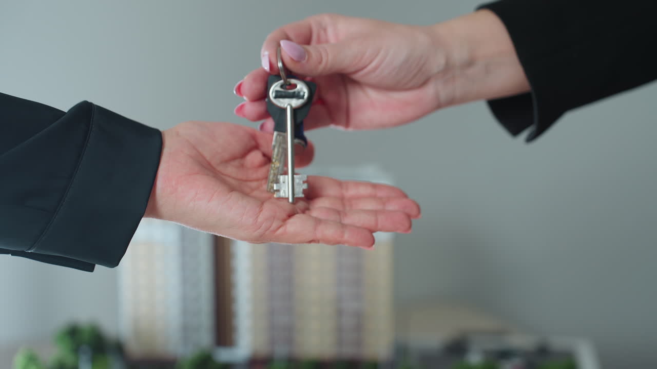 close up handover moment showing key dropped into open palm symbolizing real estate ownership or rental agreement completion with blurred building miniature in background