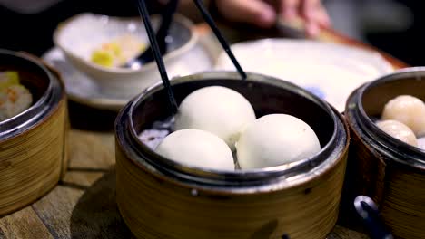 chopsticks lifting buns from bamboo steamer