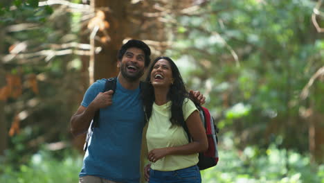 Couple-With-Backpacks-Holding-Hands-Hiking-Or-Walking-Through-Woodland-Countryside-In-Summer