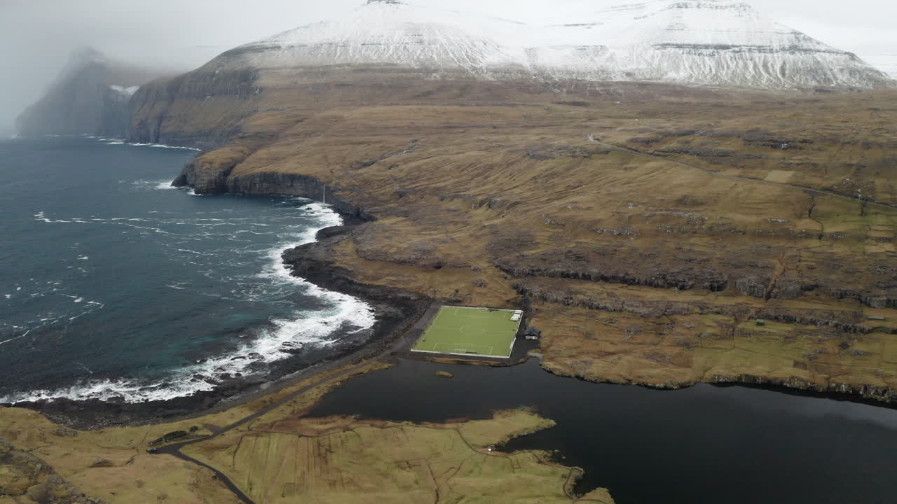 Faroe Islands, 4K Aerial Orbit of Ni&eth;ara Vatn football pitch with beautiful mountains in the background