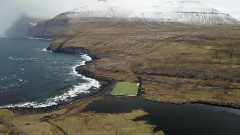 faroe islands, 4k aerial orbit of niðara vatn football pitch with beautiful mountains in the background