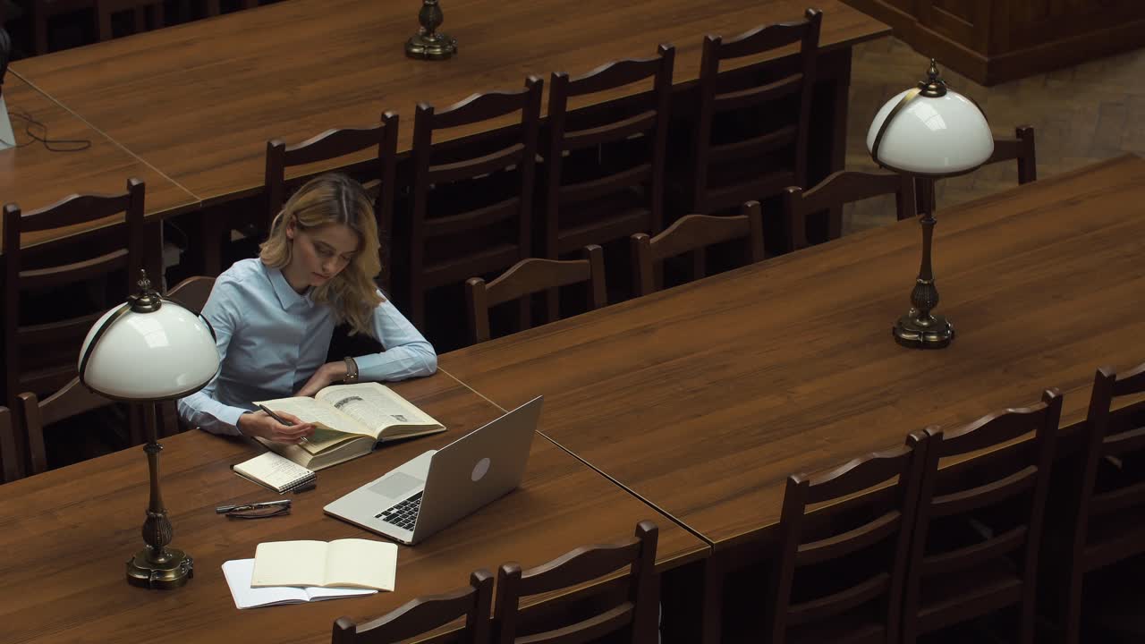 mujer leyendo un libro en la mesa de la biblioteca