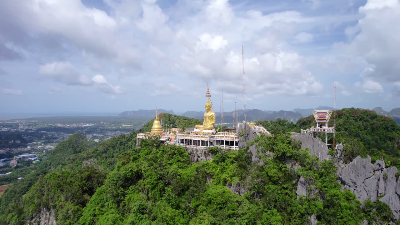 Rekaman drone udara jarak dekat Kuil Gua Harimau (Wat Tham Suea) di Krabi, Thailand, menyoroti patung Buddha emas dan kompleks kuil yang bertengger secara dramatis di puncak karst batu kapur.