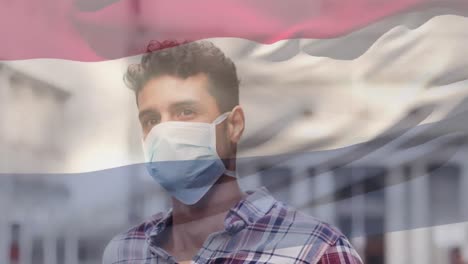Animation-of-flag-of-netherlands-waving-over-man-wearing-face-mask-during-covid-19-pandemic