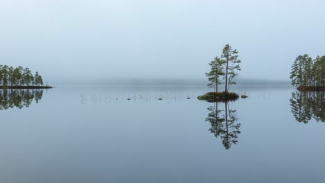 fog forming and passing over glassy lake surface with focus on trees on islet