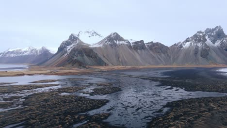 Schwarzer-Sandstrand-Bei-Ebbe-Mit-Wasserbecken-Unterhalb-Der-Bergkette