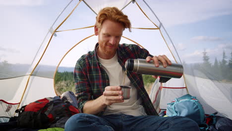 redhead man drinking hot tea in mountains