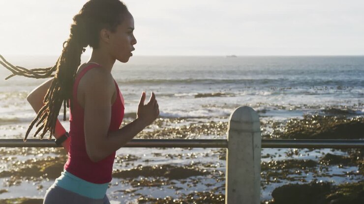 Femme afro-américaine en tenue de sport courant sur une promenade en bord de mer.