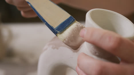 close up view of female potter using glaze brush to paint on pot at pottery studio