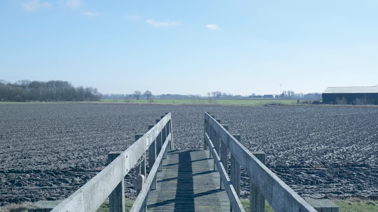 Camera Rises from Under a Wooden Bridge to Reveal a Plowed Field