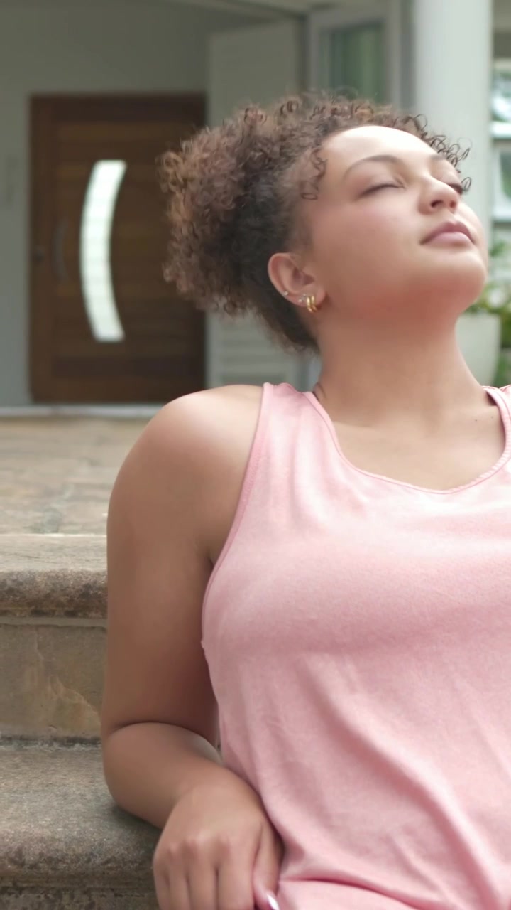 Video verticale: Panoramica che mostra una donna con un top rosa che si sposta sui gradini di pietra, sistemandosi, spazio per il testo.