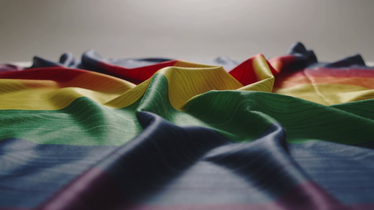 Shifting rainbow fabric forming rising center ridge as folds relaxing on flat surface, studio light