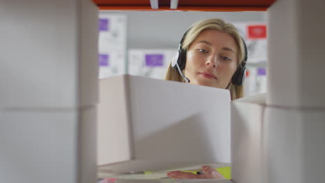 female worker wearing headset in logistics distribution warehouse putting box on shelf