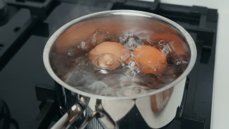 eggs boiling over gas stove in a stainless steel pot