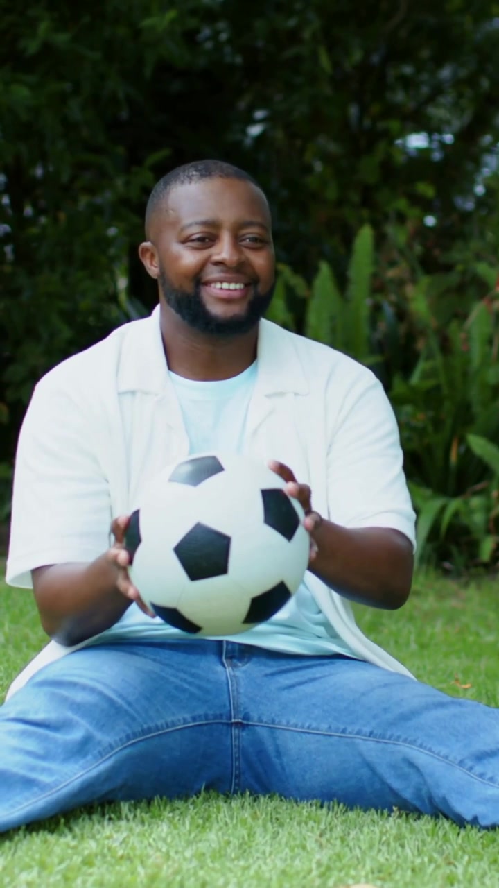 Vertical video: Catching man in tee readying soccer ball in yard after offframe toss to pass