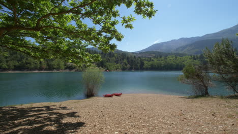 Subiendo-Desde-El-Suelo-Hacia-Un-árbol,-Vemos-Dos-Kayaks-Sentados-En-La-Orilla-Del-Lago-Tsivlos