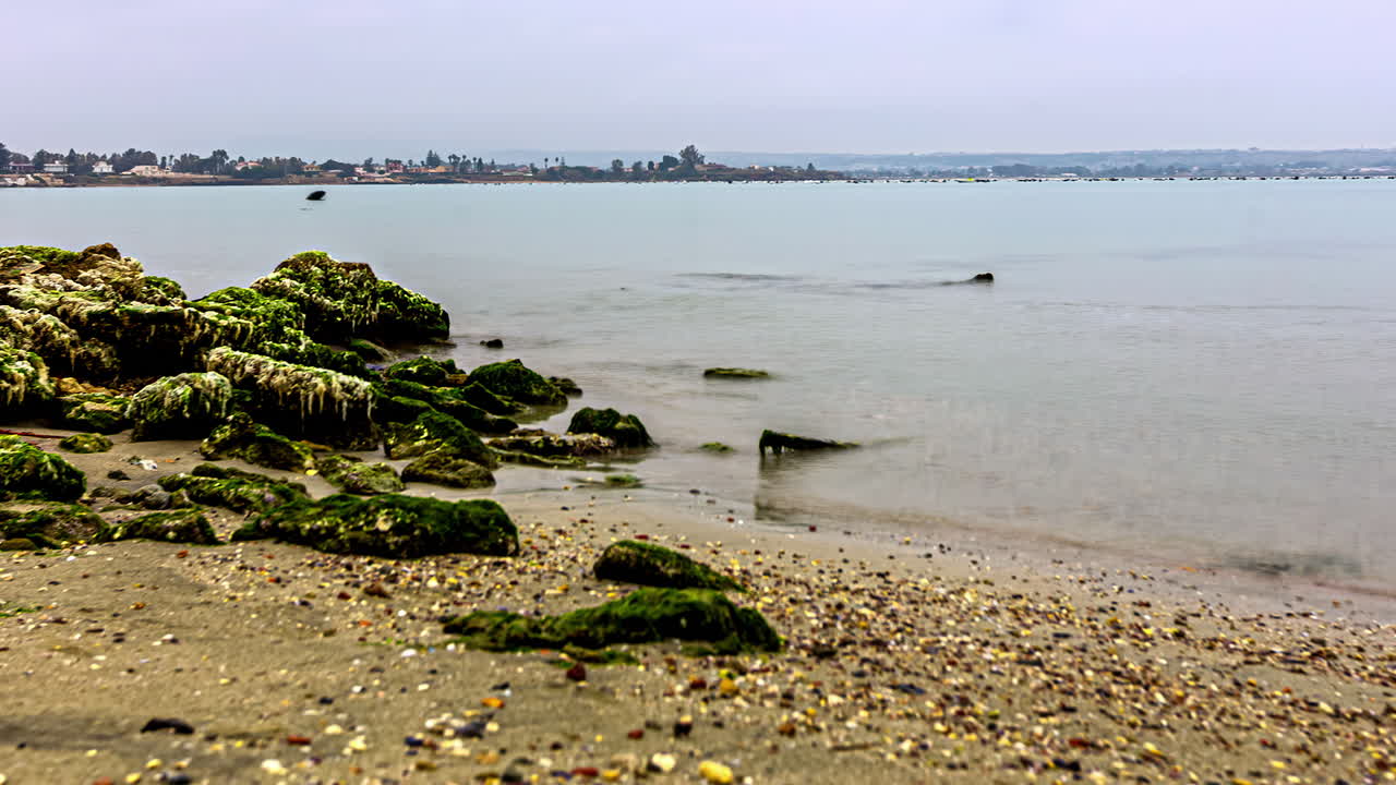 timelapse que muestra la pintoresca costa siciliana, con rocas, mar tranquilo, un barco en movimiento y la ciudad en la distancia