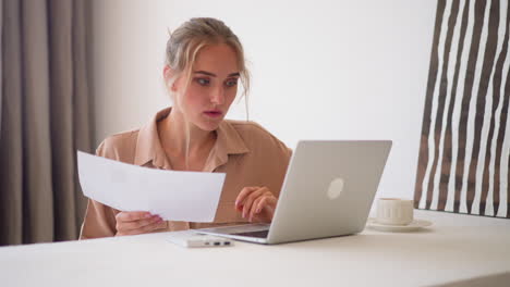 young woman does paper work looking at screen of laptop