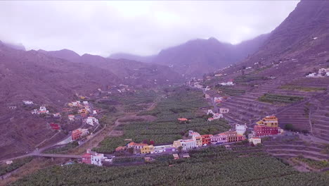 revealing aerial view of hermigua beach, valley, banana plantation, colorful houses and mountains in hermigua valley, north of la gomera, canary islands, spain on a cloudy day