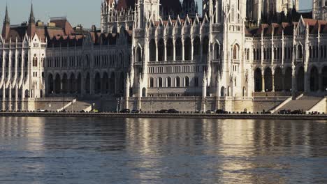 Budapest-city-center-view-with-Parliament-building-and-Danube-river-on-a-sunny-day,-gothic-architecture,-cars-moving-on-the-street,-medium-low-angle-distant-shot