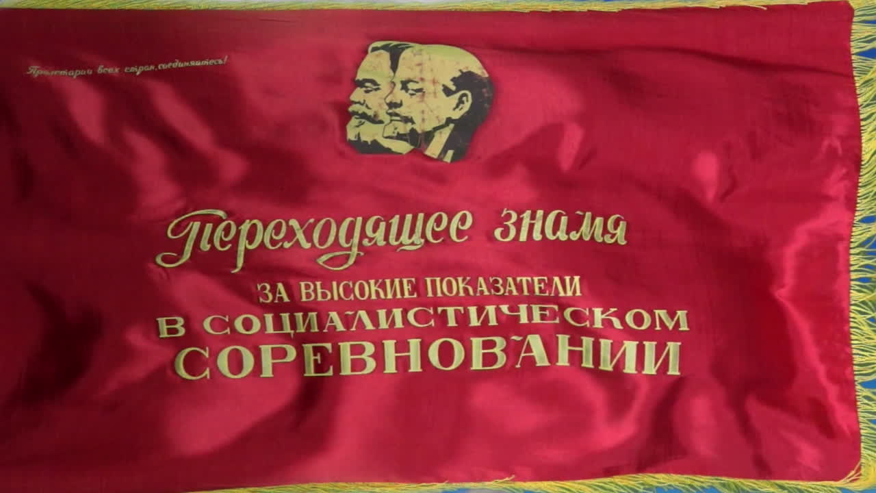 A Soviet flag depicting Marx and Lenin with the caption, &amp;quot;Transferrable Banner for High Results in Socialist Competition&amp;quot; flies against a vivid blue sky