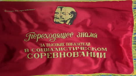 a soviet flag depicting marx and lenin with the caption, "transferrable banner for high results in socialist competition" flies against a vivid blue sky