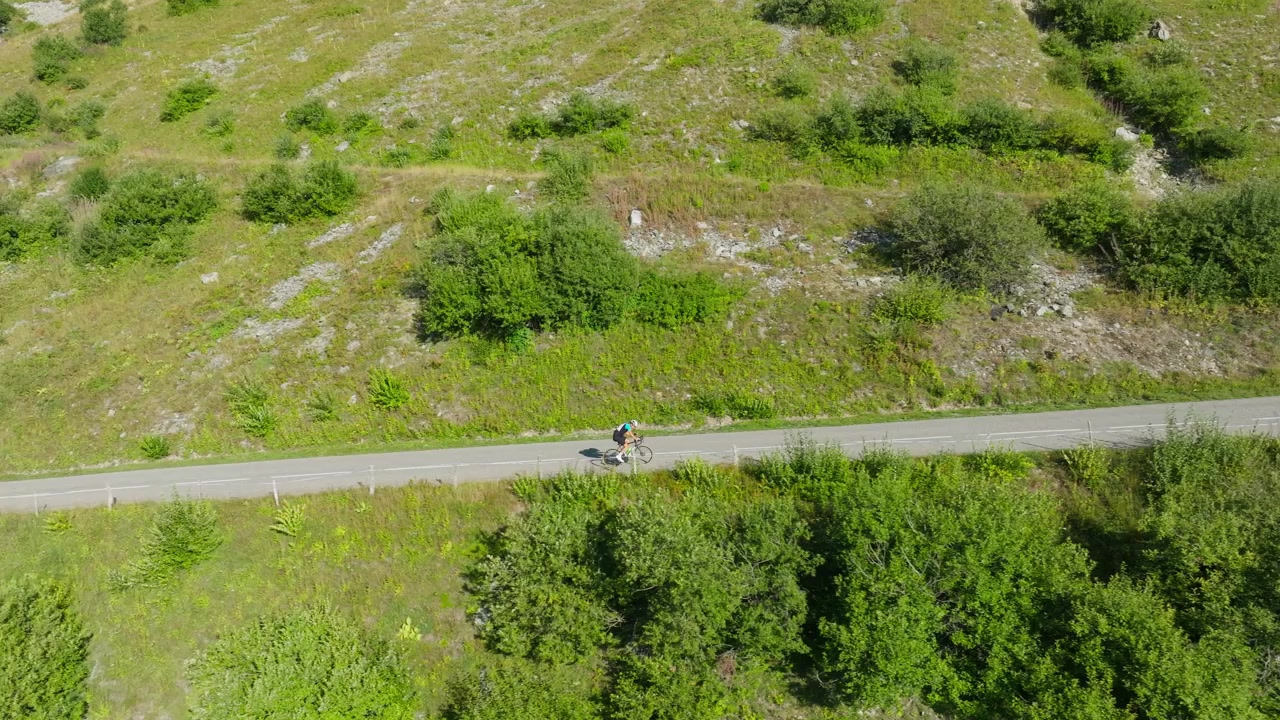 Filmisk luftdroneoptagelse af de franske Alper med betagende bjerglandskaber, snoede alpeveje, frodige grønne dale og cyklister, der kører gennem spektakulære landskaber. Perfekt til rejse.