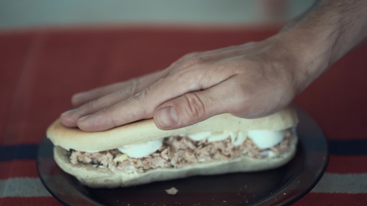 presionando un huevo con sándwich de atún, pan tostado blanco, cámara lenta 120 fps, mano masculina blanca