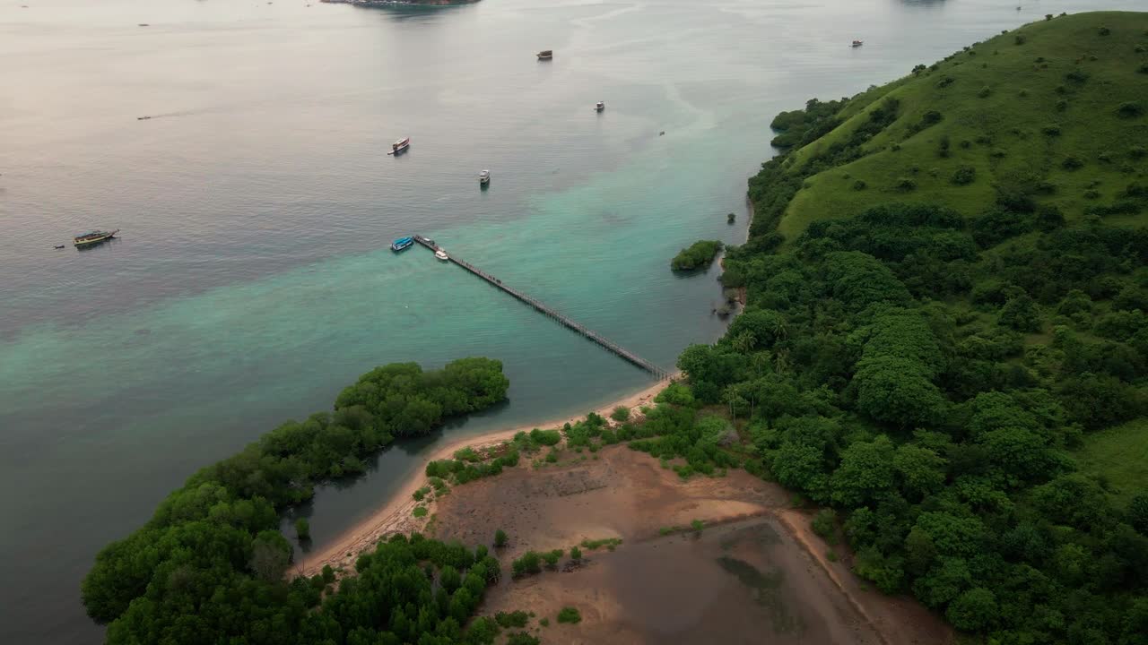 Aerial video from the hill of Komodo Island shows a beautiful, crystal-clear ocean with small islands surrounding. several boats anchored nearby the wooden pier from the bay.