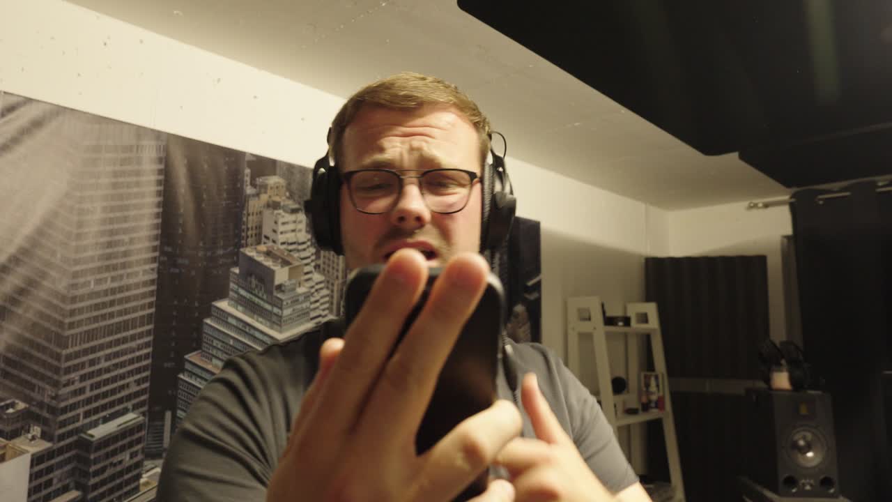 A musician wearing headphones is generating music with AI. He is holding a smartphone in his hands