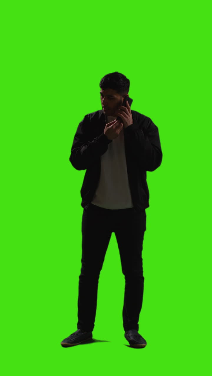 Vertical Video Full Length Shot Of Young Man Answering Call On Mobile Phone Standing Against Green Screen With Low Key Lighting 2