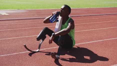 Disabled-mixed-race-man-with-prosthetic-legs-sitting-on-a-race-track-and-drinking-water