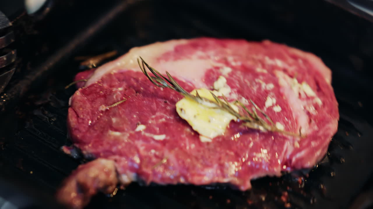 Butter melting on a seasoned steak cooking on a hot grill pan with rosemary herbs