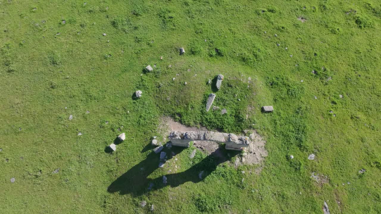 Frontal drone flight with cenital view of Puerta de Arenas and its striking arch. Around it, mounds of earth reveal the covered remains of the original stone structure under the soil.