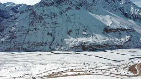 aerial shot of a man walking on a helipad covered with snow revealing huge mountains of spiti in the background