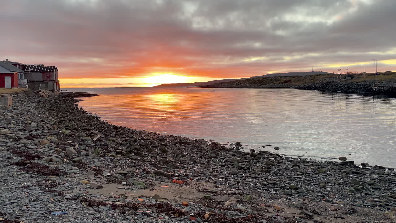 toma estática de una puesta de sol sobre una pequeña entrada del océano con una costa rocosa y casas