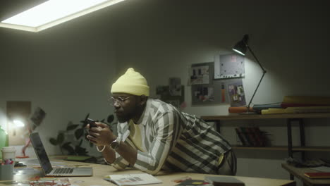 man using smartphone at a dimly lit design studio desk