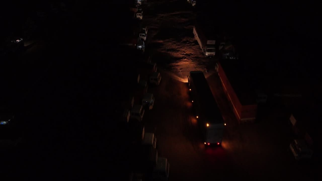 High-angle night footage of a semi-trailer truck moving slowly through a dark, industrial staging area. Ideal for logistics, security, and night commerce