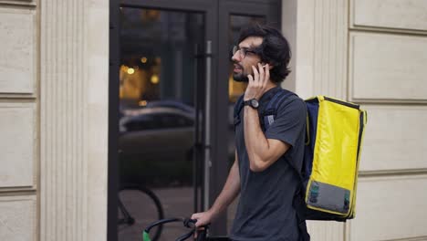 delivery man with yellow backpack talk to a client on the street using earphones, slowmo