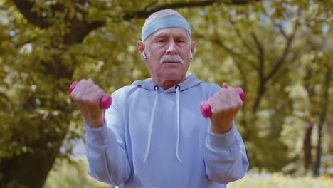 Hombre-Mayor-Haciendo-Ejercicio,-Haciendo-Ejercicios-De-Levantamiento-De-Pesas-Con-Mancuernas,-Practicando-Entrenamiento-Deportivo-En-El-Parque