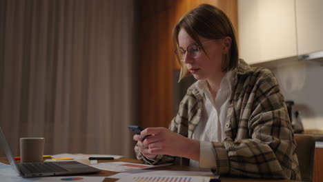 mujer joven está trabajando en casa. escribiendo en una computadora portátil y respondiendo mensajes en un teléfono. mujer usando un teléfono inteligente y relajándose en la habitación