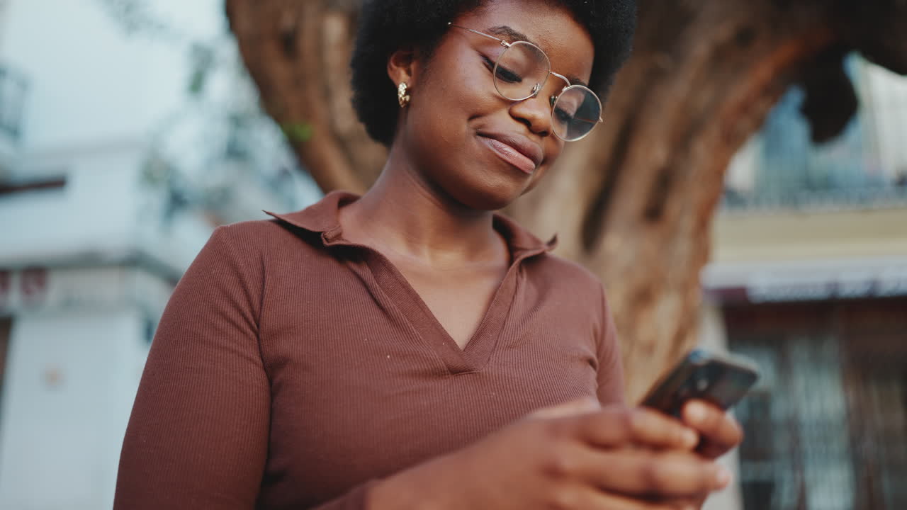 African American curly girl wearing glasses using smartphone for texting