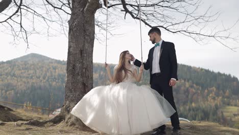 newlyweds. caucasian groom with bride ride a rope swing on a mountain slope