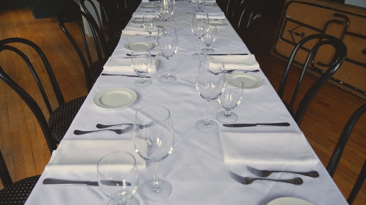 mesa de comedor para una boda o un evento corporativo en un restaurante de alta cocina platos de cerámica tenedores cuchillos servilletas de tela sobre un mantel blanco sobre la mesa a cámara lenta panorámica hasta la mesa reveladora