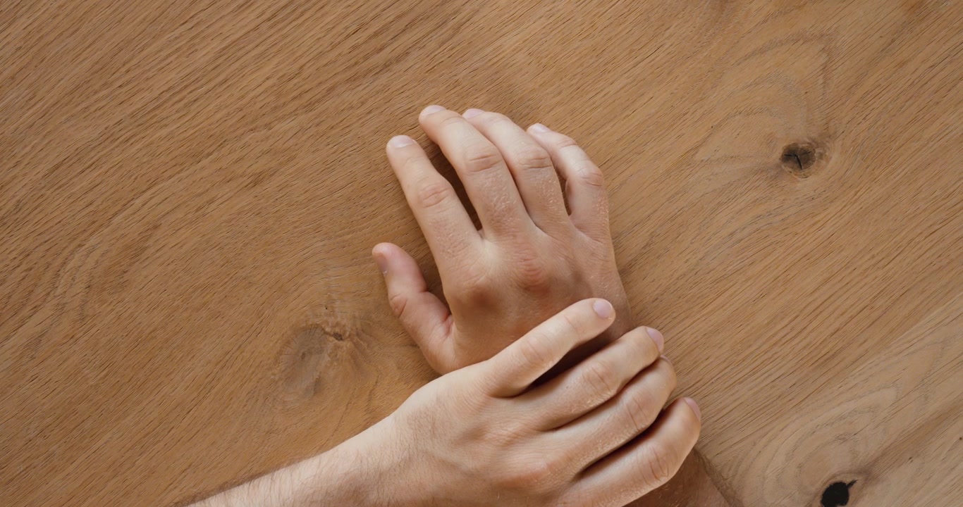 Vista dall'alto di una persona che si strofina nervosamente il polso con l'altra mano. Concetto di ansia, stress, nervosismo, tensione e linguaggio del corpo irrequieto.
