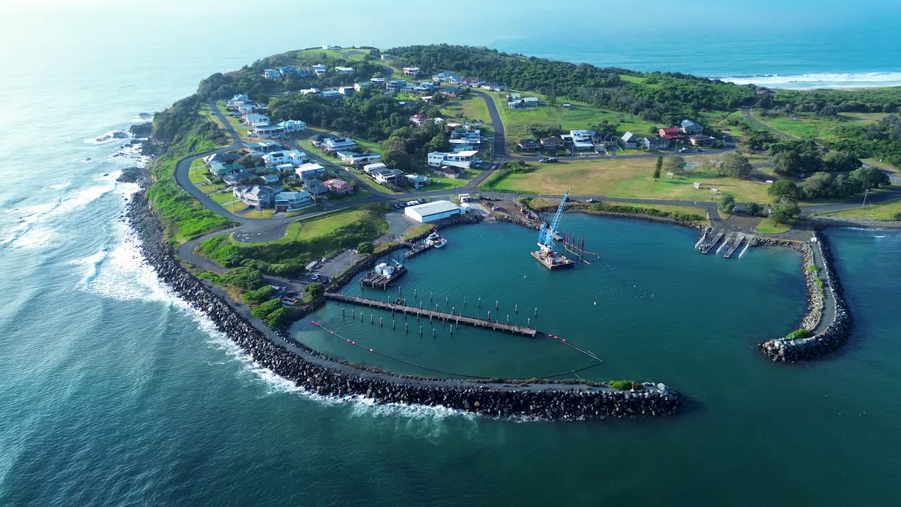 Drone aerial landscape of crane and rocky pier break wall with local town suburbs at Crowdy Head boat harbour wharf located along scenic Australian coastline headland with ocean waves travel tourism