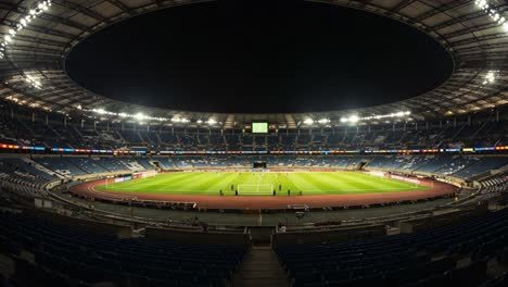 nighttime stadium overview capturing an empty arena with lush green field and bright stadium lights illuminating the surrounding seating areas