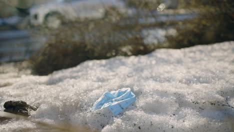 slomo pan of face mask on snowy ground in sunlight, car passes behind